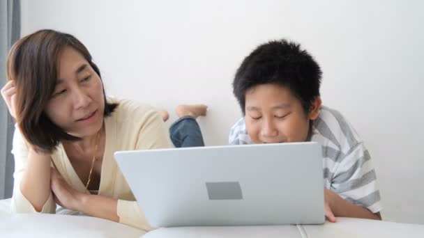 11岁的男孩躺在床上和他的母亲玩笔记本电脑 — 图库视频影像