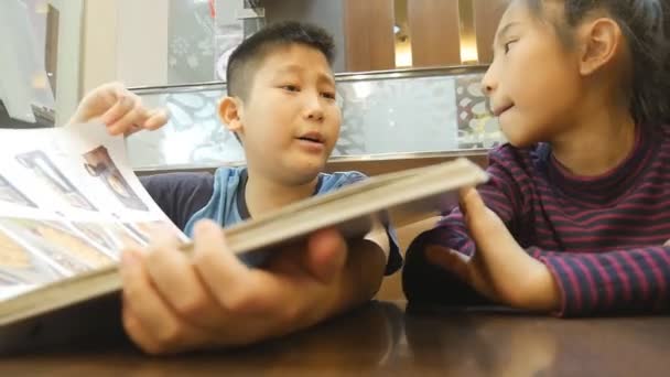 Asiatisch Süß Junge Und Mädchen Reading Menu Buch — Stockvideo