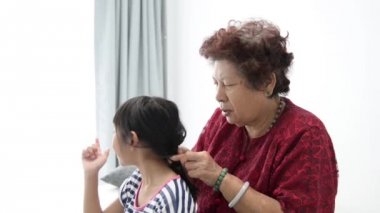 Asyalı üst düzey kadın onun torunu'nın saç, aile yaşam tarzı evde örgü.