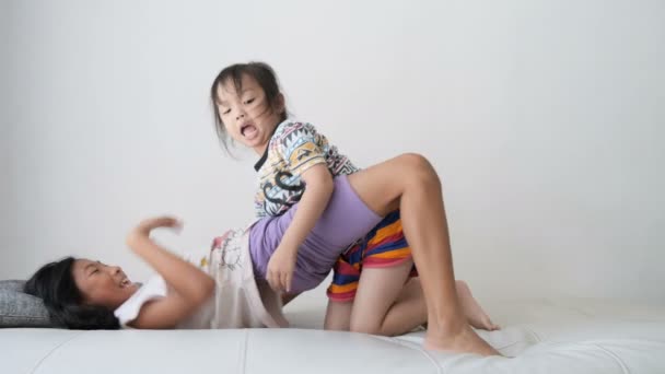 笑亚洲女孩和她的妹妹在沙发上一起玩慢动作 — 图库视频影像