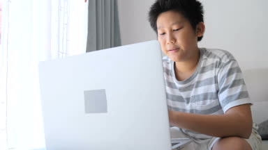 Kanepede oturan ve evde oyun oyun dizüstü kullanarak Asya varoluş çocuk.