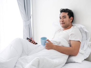 Smartphone kullanarak ve yatakta, hafta sonu kavramı adam lifestyle kahve içme gülümseyen Asyalı adam.