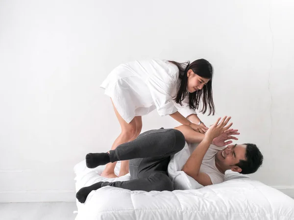 Offended man sits on the bed while the woman is standing over it waving her hands. Indoors bedroom.