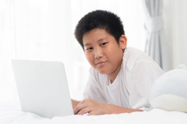 Yatakta yatarken ve dizüstü bilgisayar kullanarak mutlu Asya varoluş çocuk.