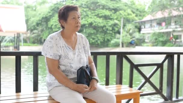 亚洲高级妇女坐在公园里看着雨落在外面 — 图库视频影像
