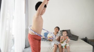 Şişman çocuk hula hoop evde oynarken yavaş göbek hareket ile. Onun kız kardeşi tezahürat için egzersiz.