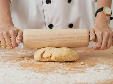 Aşçı elleri ahşap tahtada hamurdan bir kruvasan yuvarlıyor. siyah arkaplan.