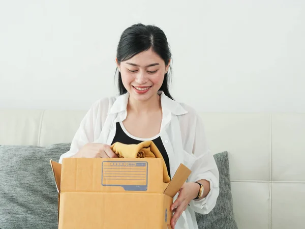 delivery, mail and people concept - smiling Asian woman opening cardboard box at home.