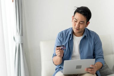 Asya adam alışveriş online kredi kartı ve dizüstü bilgisayar basılı tutup evde oturan yaşam tarzı kavramı ile.