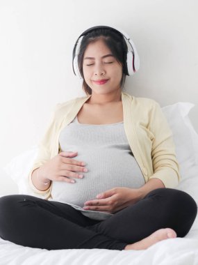 Kulaklık müzik dinleme yatak, yaşam kavramı kullanarak Asya pragnant kadın.