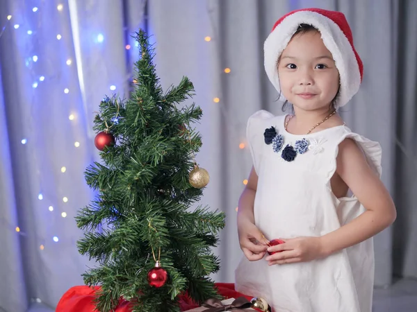 サンタの帽子を自宅のクリスマス ツリーを飾ると幸せなアジアの女の子 — ストック写真