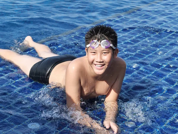 快乐的亚洲男孩戴着护目镜 躺在游泳池在阳光明媚的日子 生活方式的概念 — 图库照片