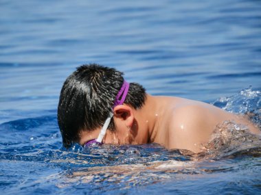 Asyalı çocuk giyiyor koruyucu gözlük ve güneşli bir günde, havuzda nefes öğrenme bulanıklık hareket.