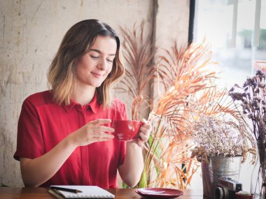 Güzel kadın çalışırken kafeteryasında kırmızı fincan kahve içme.