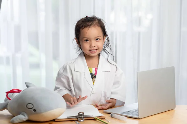 亚洲女孩玩医生和使用笔记本电脑在家里的桌子上 — 图库照片