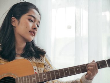 Evde, gitar çalmak mutlu Asyalı kadın yaşam tarzı kavramı.