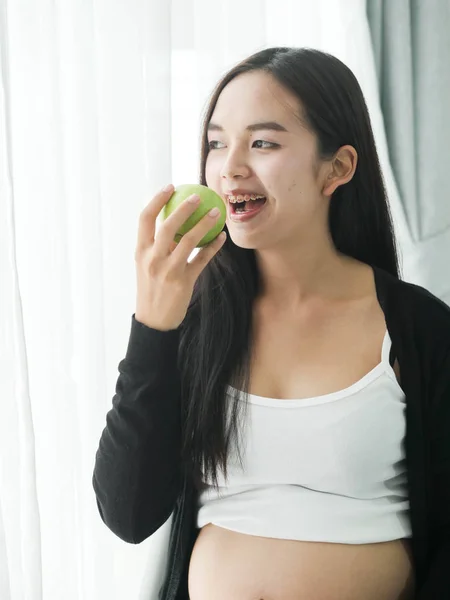 Mulher Asiática Feliz Comer Maçã Verde Perto Janela Casa Conceito — Fotografia de Stock
