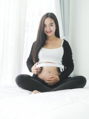 Güzel Asyalı hamile kadın kulaklık karnı üzerinde evde, yaşam kavramı kullanarak.