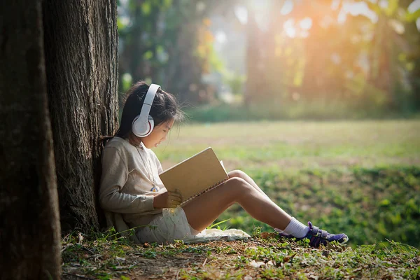 Aziatisch Meisje Met Boek Hoofdtelefoon Aanbrengen Onder Grote Boom Ochtend — Stockfoto