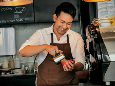 Latte sanat için kırmızı kahve fincanı içine süt dökme mutlu Asya barista.