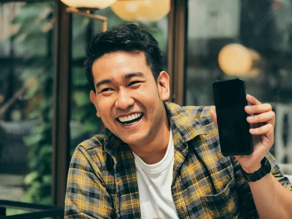 Happy Asian man pointing to black smart phone in his hand.