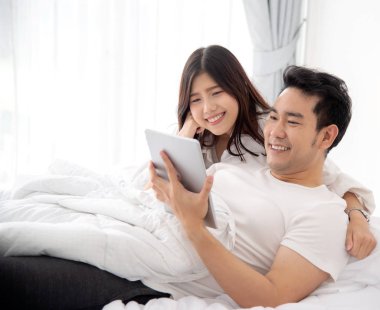 Dizüstü ve tablet birlikte yatağa evde, yaşam kavramı kullanarak mutlu Asya çift.