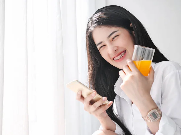 Glad asiatisk kvinna med smartphone och hålla ett glas apelsin — Stockfoto