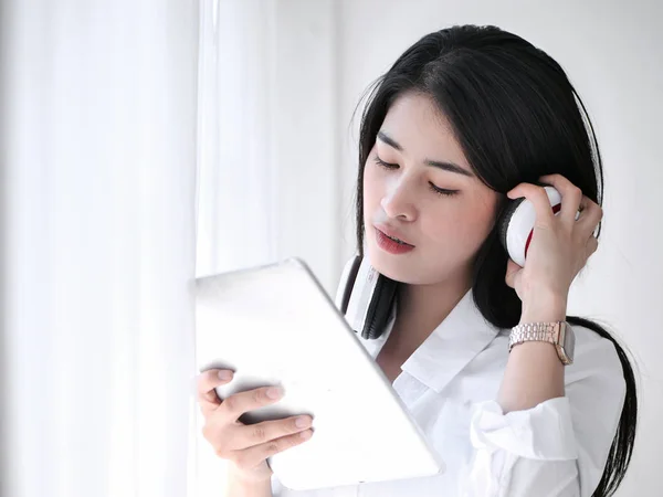 Hermosa mujer asiática usando auriculares y tabletas cerca de la ventana en — Foto de Stock
