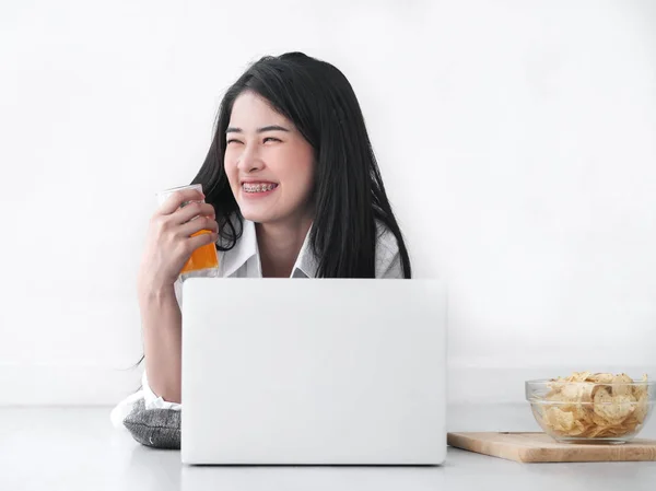 Азиатка в белой рубашке пьет стакан апельсинового сока — стоковое фото