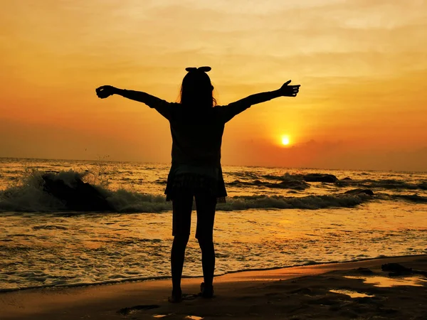 Silhueta menina levantando as mãos na praia ao nascer do sol . — Fotografia de Stock