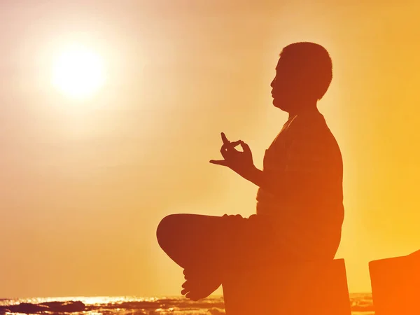 Silhouette preteen boy doing meditation on the beach in sun rise