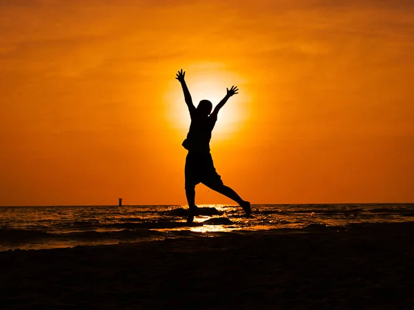 Silhouette boy jumping and raising hands on the beach in sun ris — Stock Photo, Image