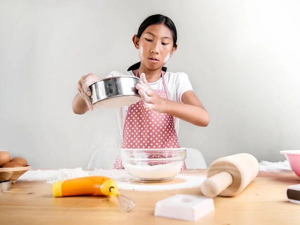 Asian girl sprinkling powder flour in bowl, bakery processing.