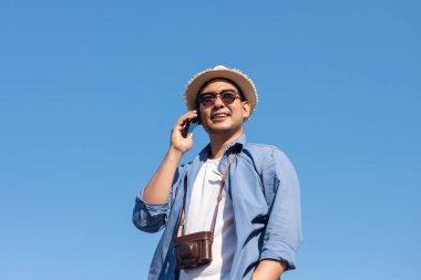 Turist Asya adam cep telefonu mavi gökyüzü ile yaz aylarında konuşurken. 