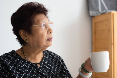 Asyalı kadın kıdemli sıcak aydınlık penceresiyle yakınındaki bir fincan çay içmek