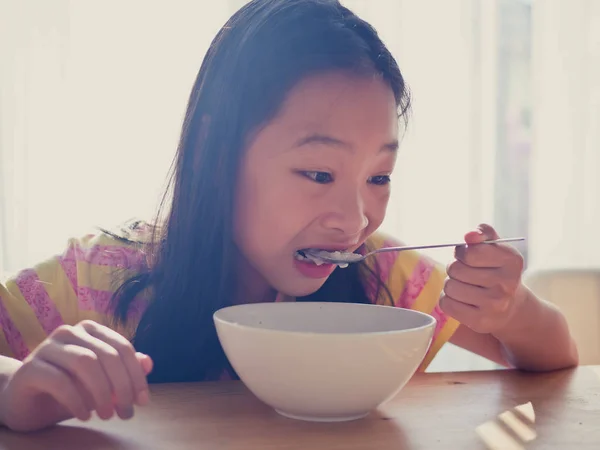 Cute Asian dívka jí rýže polévka k snídani — Stock fotografie