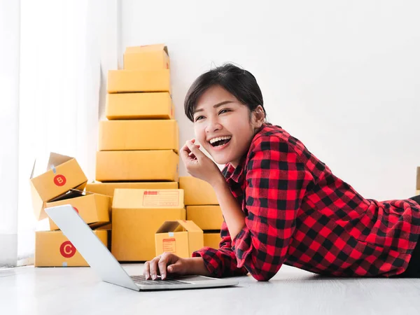 Mujer asiática acostada en el suelo y el uso de ordenador portátil con paquete marrón b —  Fotos de Stock