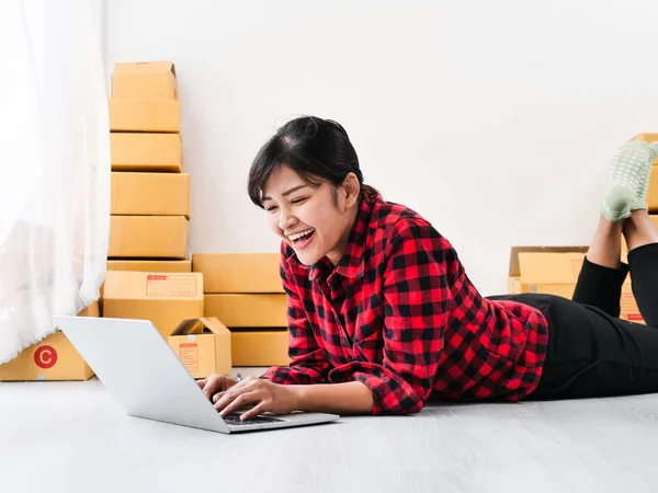 Asian woman laying on floor and using laptop with parcel brown b