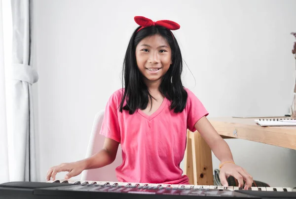 Asiatico ragazza giocare tastiera pianoforte vicino finestra a casa . — Foto Stock