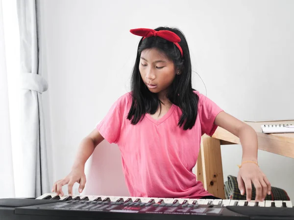 Menina asiática tocando piano teclado perto da janela em casa . — Fotografia de Stock