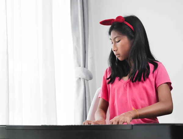 Asiático chica jugando teclado piano cerca ventana en casa . — Foto de Stock