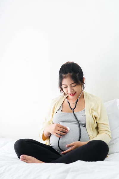 Asiatico incinta donna utilizzando stetoscopio ascoltando il suo bambino su letto — Foto Stock