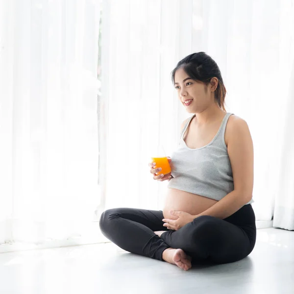 Asiático mulher grávida segurando um copo de suco de laranja e sentado — Fotografia de Stock