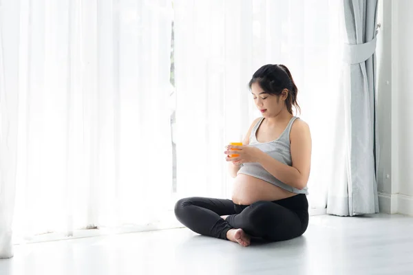 Asiático mulher grávida segurando um copo de suco de laranja e sentado — Fotografia de Stock