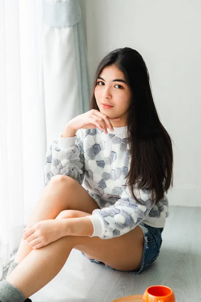 Nachdenkliche asiatische Teenager sitzen auf dem Boden in der Nähe Fenster mit ora — Stockfoto