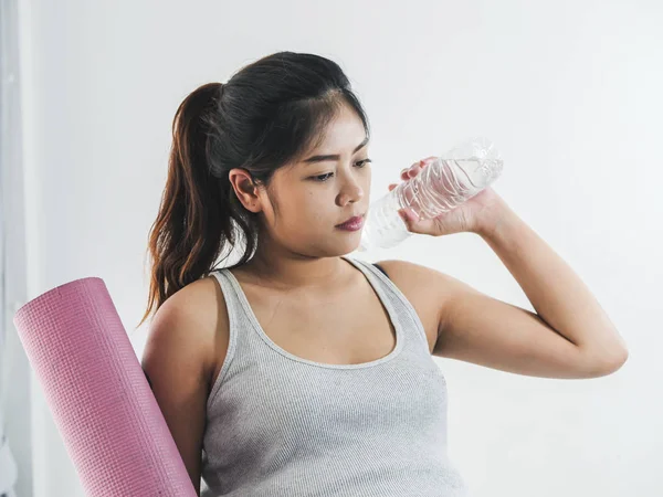 Asian pregnant woman holding pink yoga mat and a bottle of water