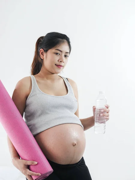 Mulher grávida asiática segurando tapete de ioga rosa e uma garrafa de água — Fotografia de Stock