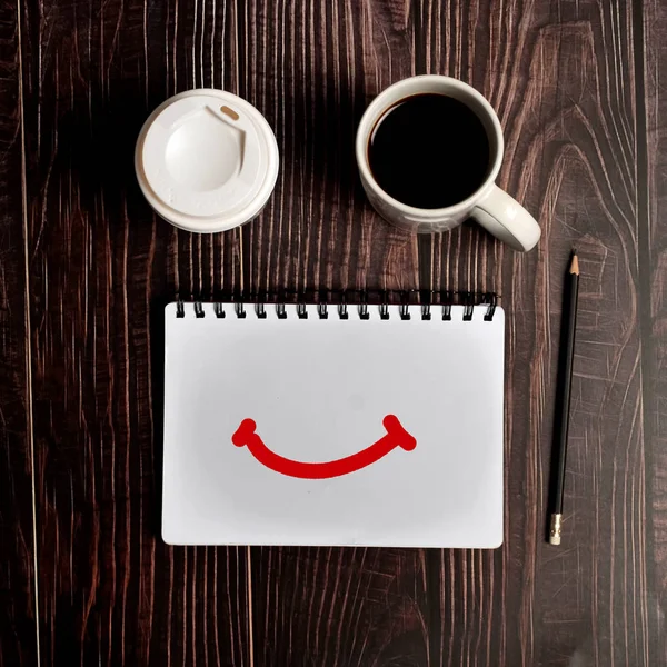 Bloco de notas de rosto sorridente com caneca de café em marrom textura de madeira backg — Fotografia de Stock