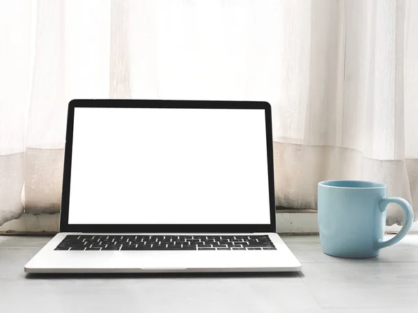 Vit skärm bärbar dator, blå kaffemugg på grå trä flik — Stockfoto