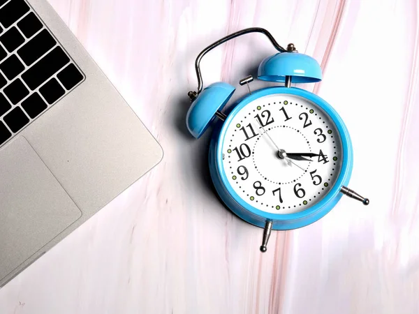 Blue alarm clock and laptop on marble background, concept.